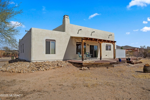 rear view of house with a chimney, a patio area, and stucco siding