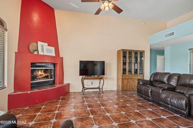 living area featuring ceiling fan, a towering ceiling, a glass covered fireplace, and visible vents