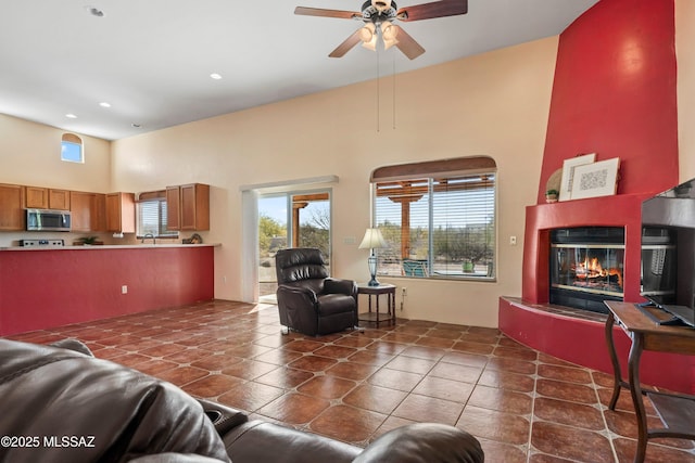 living area featuring ceiling fan, tile patterned flooring, recessed lighting, a towering ceiling, and a glass covered fireplace