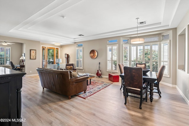 living area with a tray ceiling, visible vents, light wood-style flooring, and baseboards