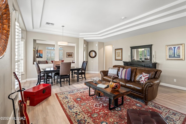 living area with a tray ceiling, light wood-style flooring, and visible vents