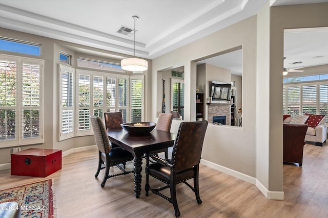 dining space with a fireplace, visible vents, baseboards, light wood finished floors, and a tray ceiling