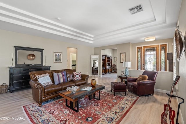 living area with light wood-type flooring, visible vents, a tray ceiling, and baseboards