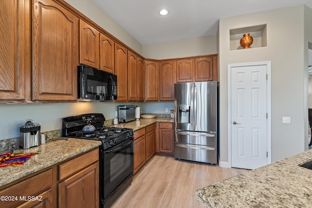 kitchen featuring brown cabinets, light wood finished floors, recessed lighting, light stone countertops, and black appliances