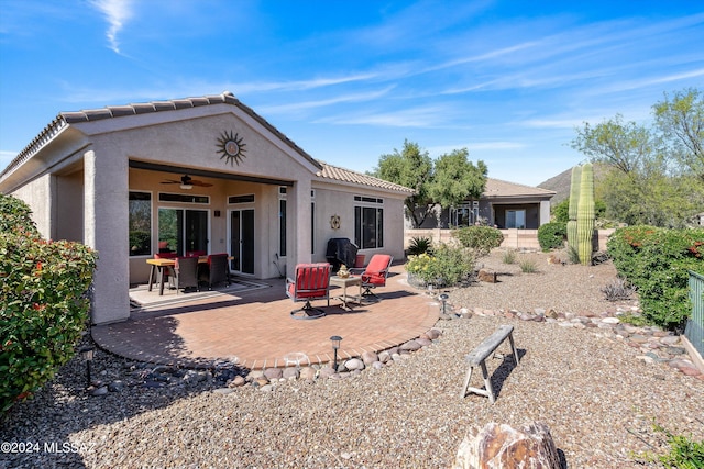 rear view of property featuring stucco siding, a ceiling fan, a patio area, fence, and a tiled roof