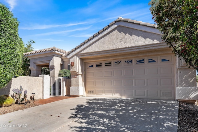 view of front of home with stucco siding, an attached garage, a gate, driveway, and a tiled roof