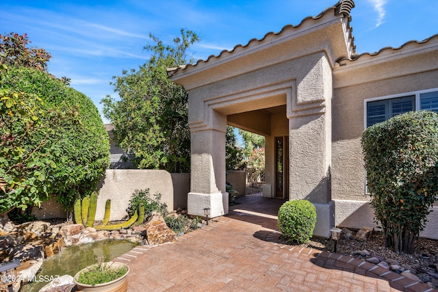 property entrance featuring a tiled roof, fence, and stucco siding