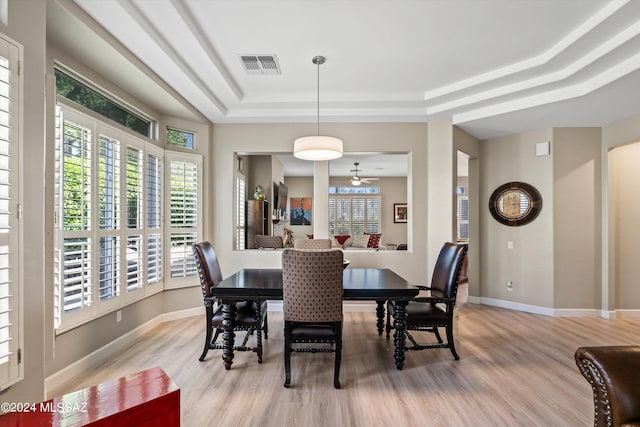 dining space with light wood finished floors, a raised ceiling, visible vents, and baseboards