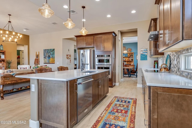 kitchen featuring stainless steel appliances, a sink, visible vents, ventilation hood, and backsplash