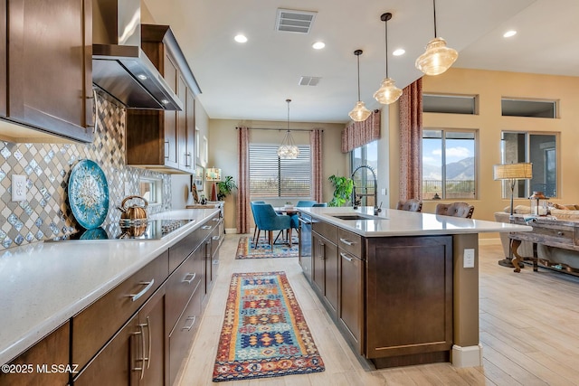 kitchen with visible vents, a sink, light countertops, wall chimney range hood, and backsplash