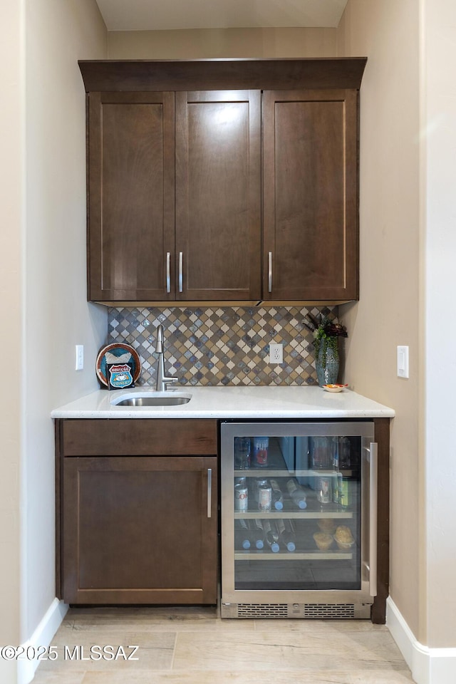 bar featuring beverage cooler, baseboards, tasteful backsplash, and a sink