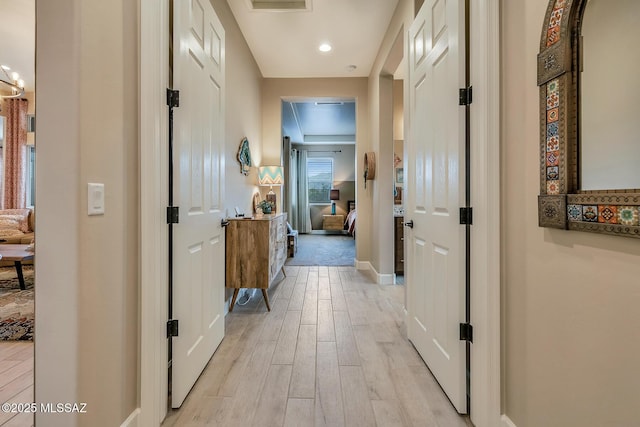 hallway with light wood-type flooring, visible vents, and baseboards