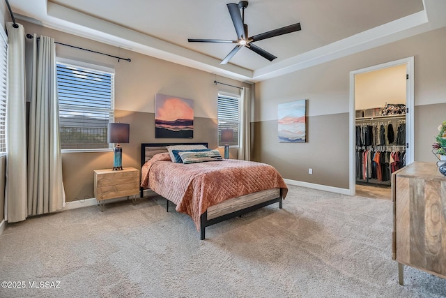 bedroom with carpet floors, a tray ceiling, a walk in closet, and baseboards