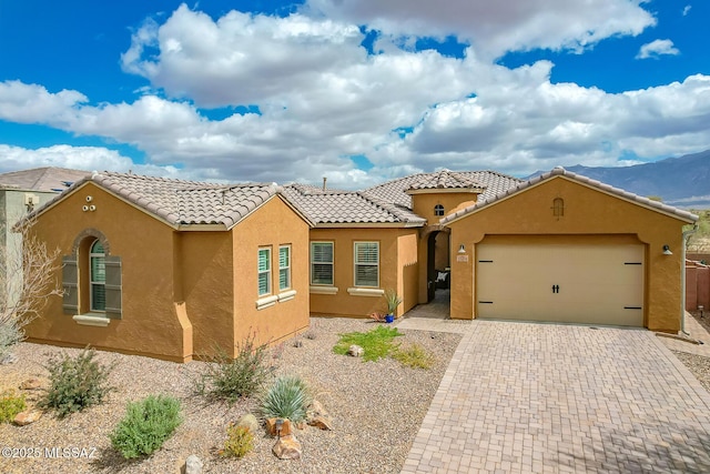 mediterranean / spanish-style home with a garage, a tiled roof, decorative driveway, and stucco siding