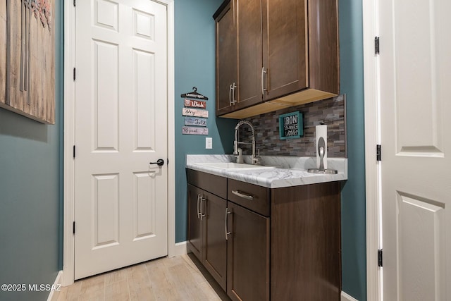 interior space featuring tasteful backsplash, light wood-style floors, a sink, and baseboards