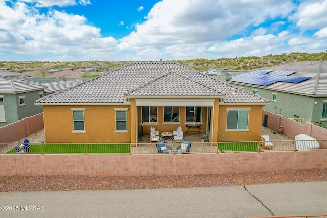 rear view of house with a patio area, a tile roof, and a fenced backyard