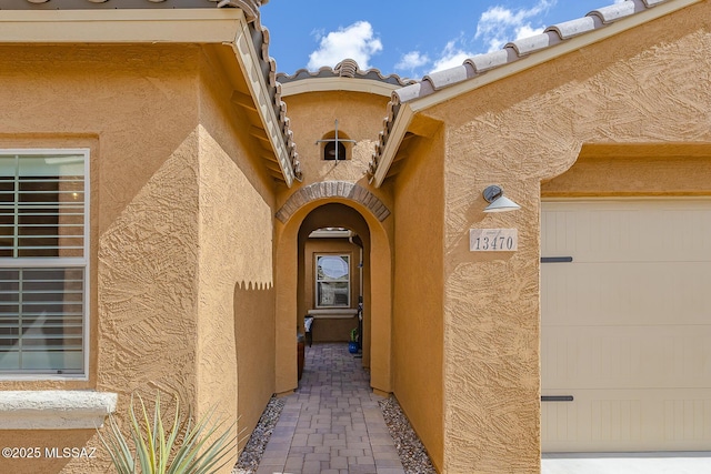 doorway to property with a tile roof, an attached garage, and stucco siding