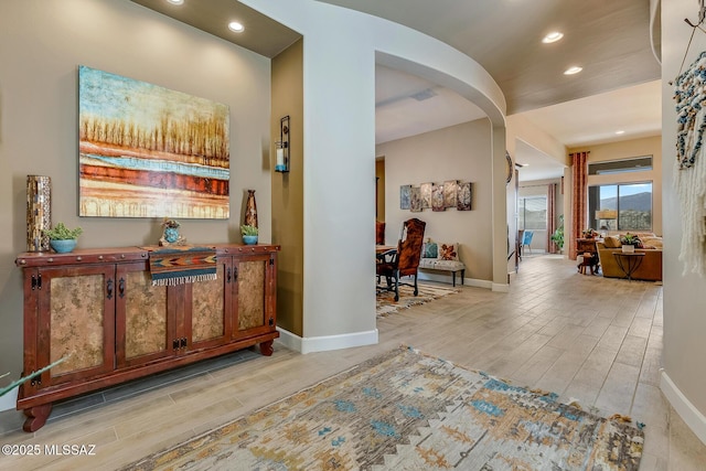 hall featuring wood finish floors, arched walkways, baseboards, and recessed lighting