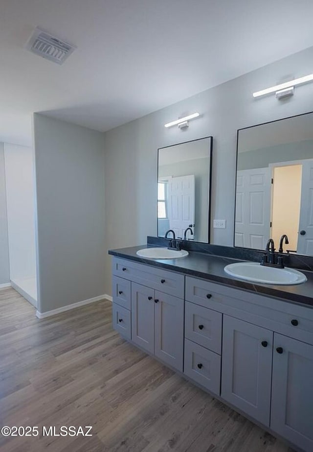 full bath featuring double vanity, wood finished floors, a sink, and visible vents