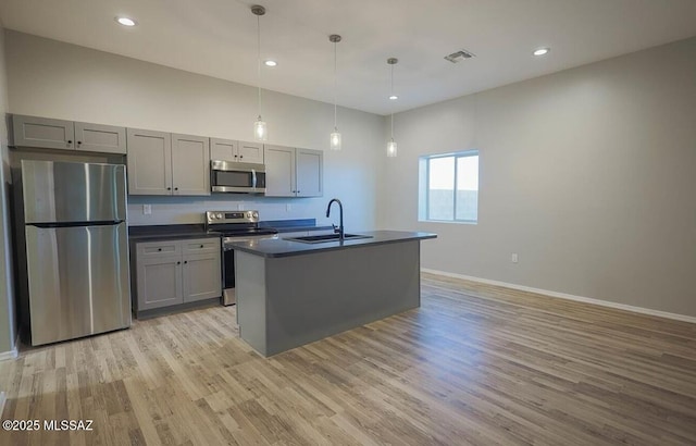 kitchen featuring decorative light fixtures, stainless steel appliances, dark countertops, gray cabinetry, and a sink