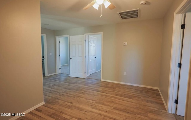 unfurnished room featuring light wood-style floors, baseboards, visible vents, and ceiling fan