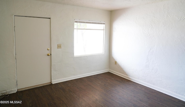 spare room with baseboards, wood finished floors, and a textured wall