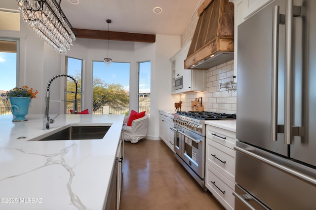 kitchen featuring premium range hood, a sink, high quality appliances, white cabinets, and decorative light fixtures