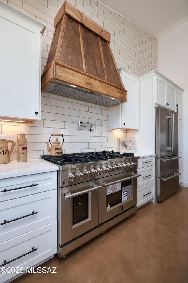 kitchen featuring high end appliances, white cabinets, premium range hood, and backsplash