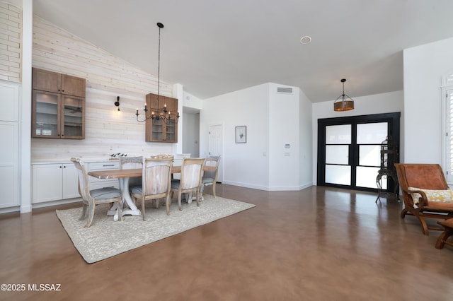 dining area with finished concrete floors, a chandelier, high vaulted ceiling, and wooden walls