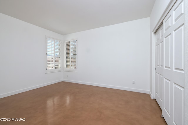 unfurnished bedroom featuring concrete flooring, a closet, and baseboards