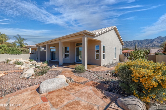 rear view of property featuring stucco siding, a mountain view, a patio, and fence