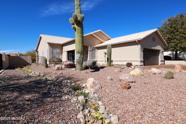 single story home featuring a garage, fence, a tile roof, and stucco siding