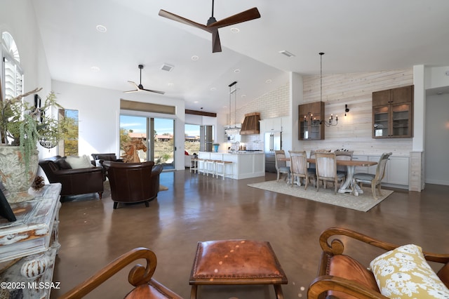 living room with ceiling fan with notable chandelier, high vaulted ceiling, visible vents, and finished concrete floors