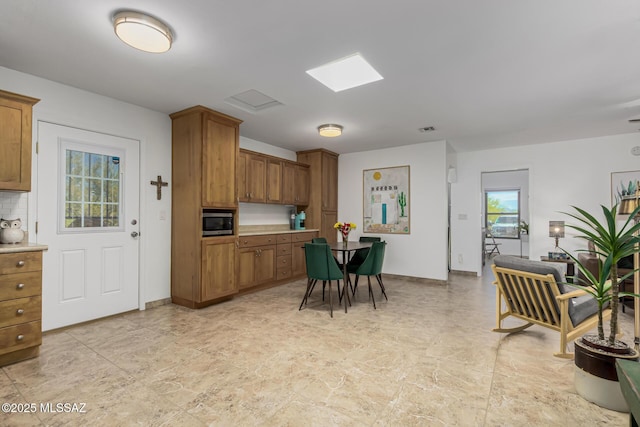 kitchen with tasteful backsplash, stainless steel microwave, visible vents, light countertops, and brown cabinets