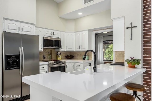 kitchen featuring backsplash, a kitchen bar, appliances with stainless steel finishes, a peninsula, and white cabinetry