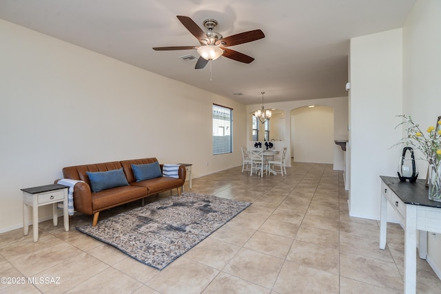 living area featuring light tile patterned floors, arched walkways, ceiling fan with notable chandelier, visible vents, and baseboards