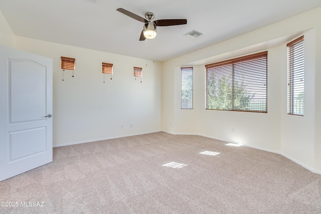 spare room featuring light carpet, visible vents, a ceiling fan, and baseboards