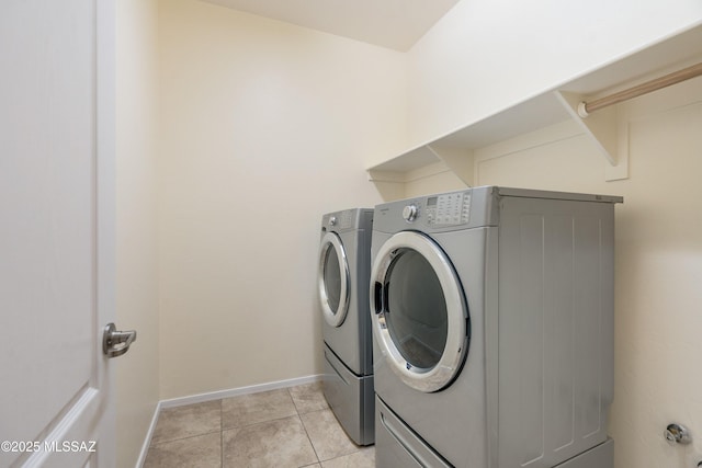 washroom featuring washing machine and dryer, laundry area, light tile patterned flooring, and baseboards