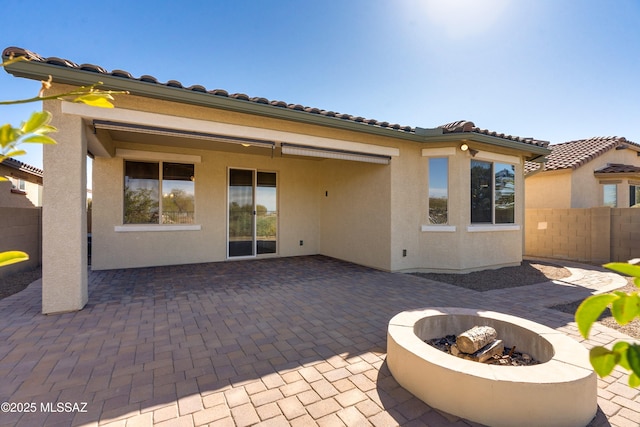 back of property featuring a patio, a fire pit, a tile roof, fence, and stucco siding