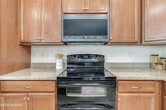 kitchen with light stone counters, brown cabinetry, stainless steel microwave, and electric range