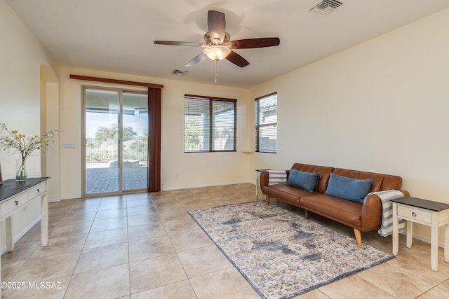 living area featuring light tile patterned floors, arched walkways, visible vents, and a ceiling fan