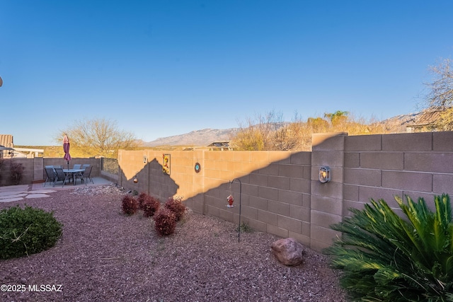 view of yard featuring a fenced backyard, a mountain view, outdoor dining area, and a patio