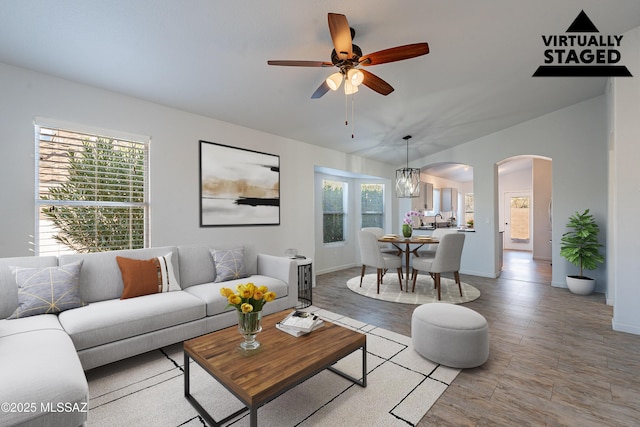 living room featuring a ceiling fan, a wealth of natural light, arched walkways, and baseboards