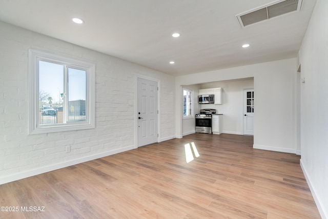 foyer featuring light wood finished floors, visible vents, baseboards, brick wall, and recessed lighting