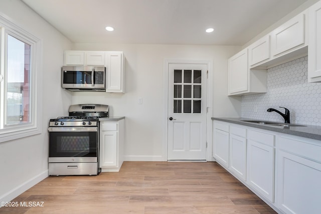 kitchen featuring appliances with stainless steel finishes, light wood-type flooring, a sink, and white cabinetry