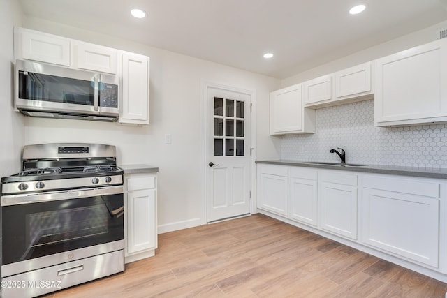 kitchen with stainless steel appliances, white cabinets, a sink, and light wood finished floors