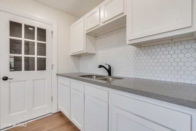 kitchen with tasteful backsplash, stone counters, white cabinetry, and a sink