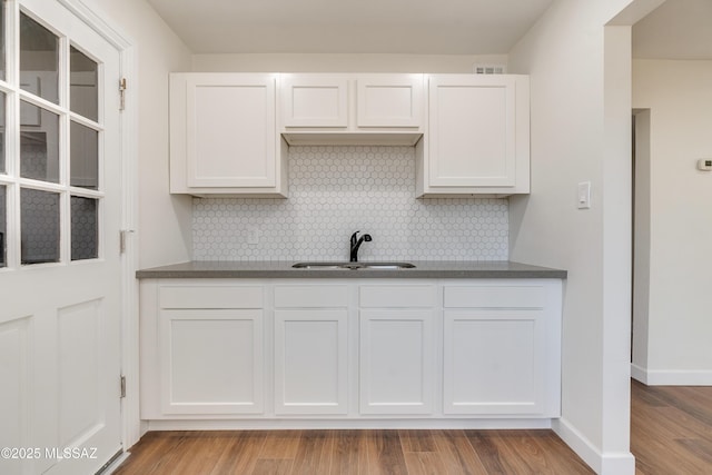 kitchen with light wood-type flooring, dark countertops, a sink, and white cabinetry