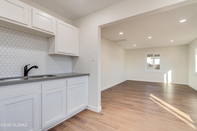 kitchen with light wood-style floors, dark countertops, white cabinetry, and a sink