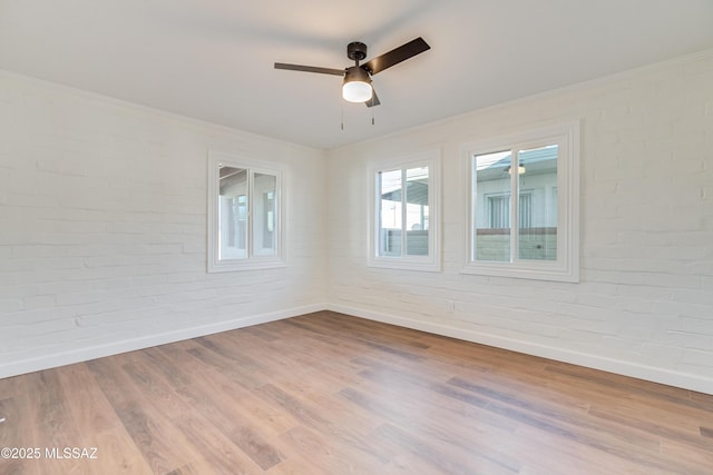 unfurnished room featuring ornamental molding, brick wall, light wood-style flooring, and baseboards